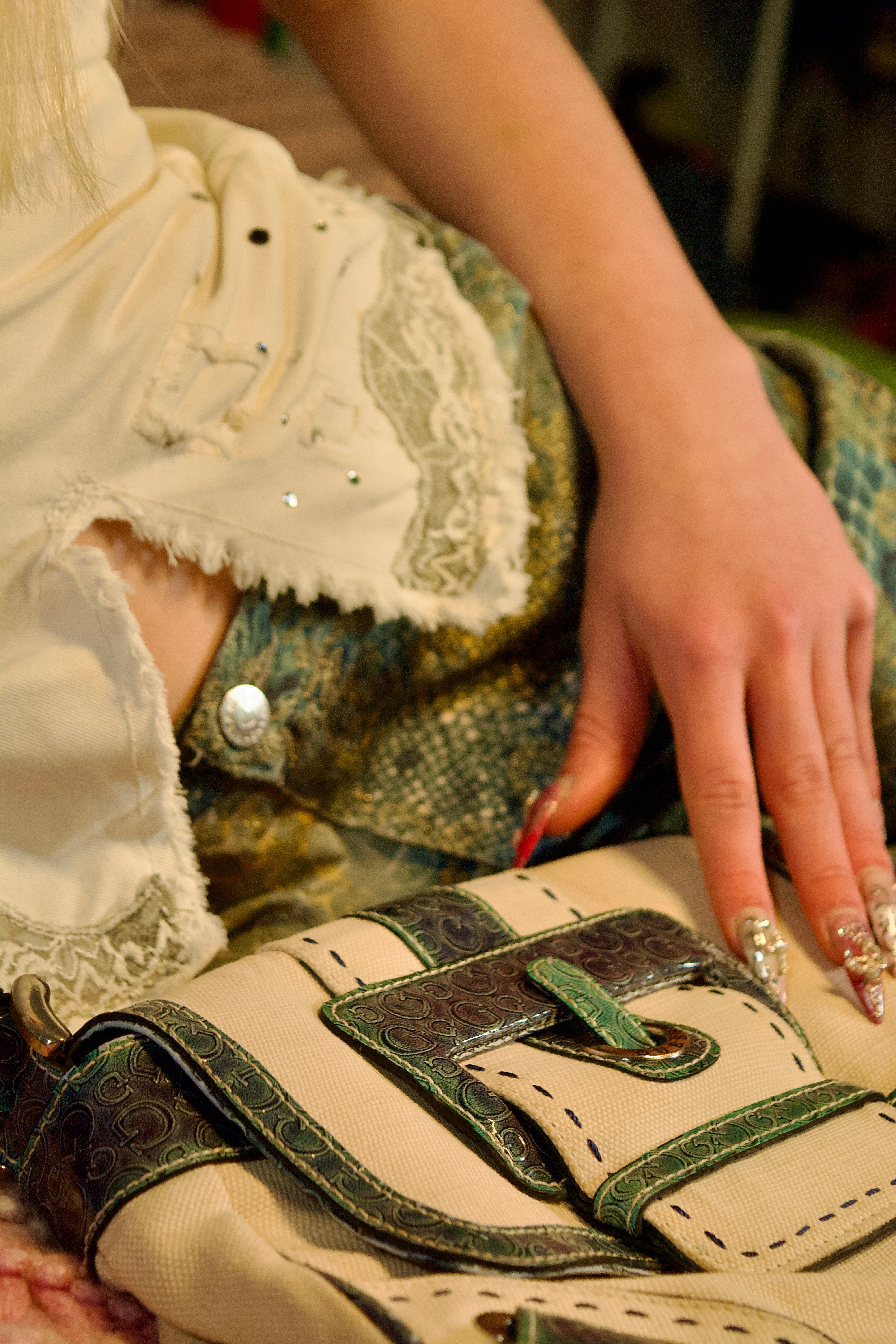 Close-up of a hand with decorative nails on a beige bag with green accents.