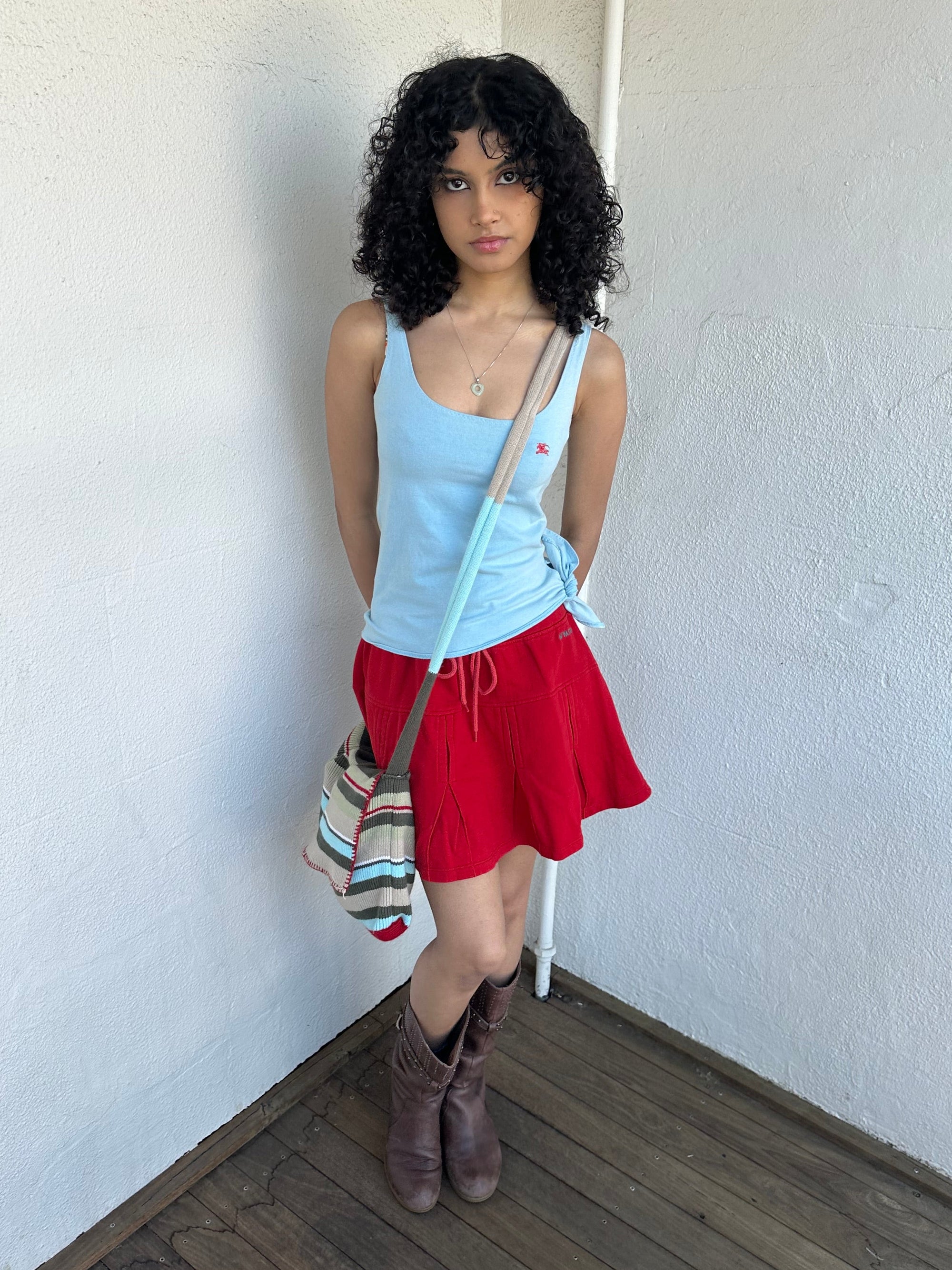 Woman wearing a Y2K 00s Multi coloured knitted satchel bag features a mix of baby blue, red, and khaki tones in a textured knit design.