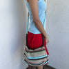 Woman wearing a Y2K 00s Multi coloured knitted satchel bag features a mix of baby blue, red, and khaki tones in a textured knit design.
