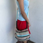 Woman wearing a Y2K 00s Multi coloured knitted satchel bag features a mix of baby blue, red, and khaki tones in a textured knit design.