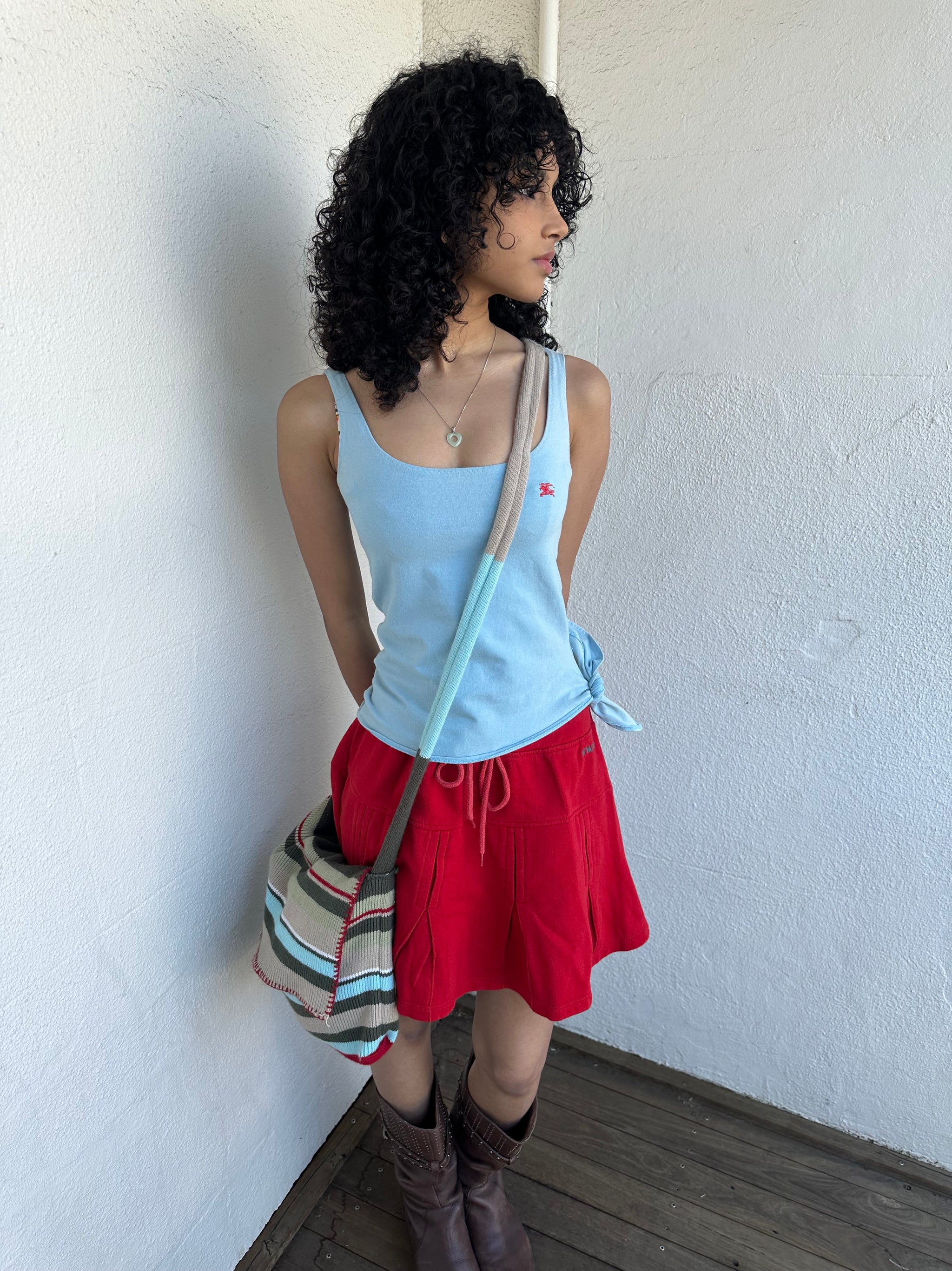 Woman wearing a Y2K 00s Multi coloured knitted satchel bag features a mix of baby blue, red, and khaki tones in a textured knit design.
