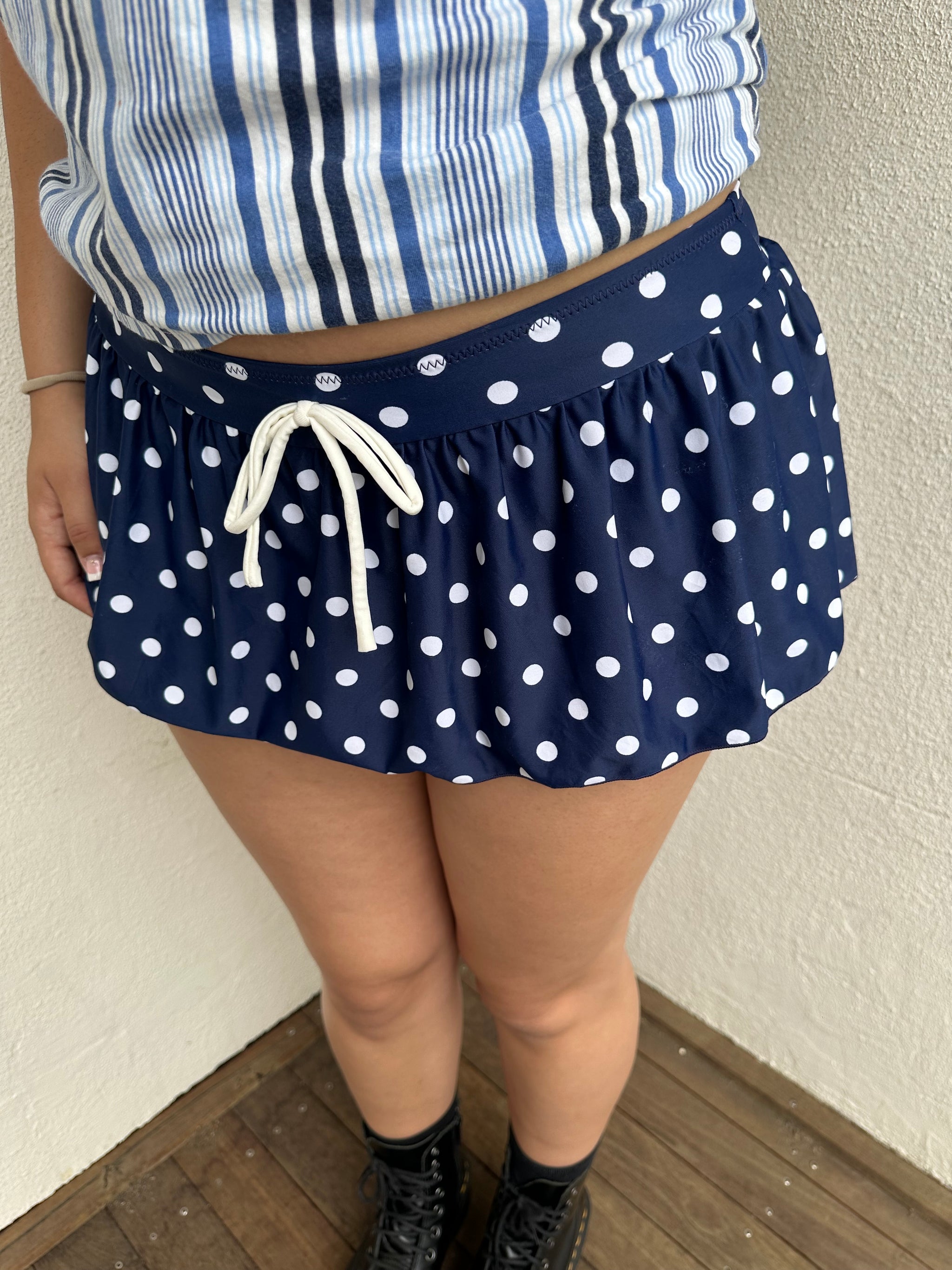 Woman Dressed in Y2K 00s Navy polkadot mini skort featuring a classic navy base with white polkadot detailing. 

