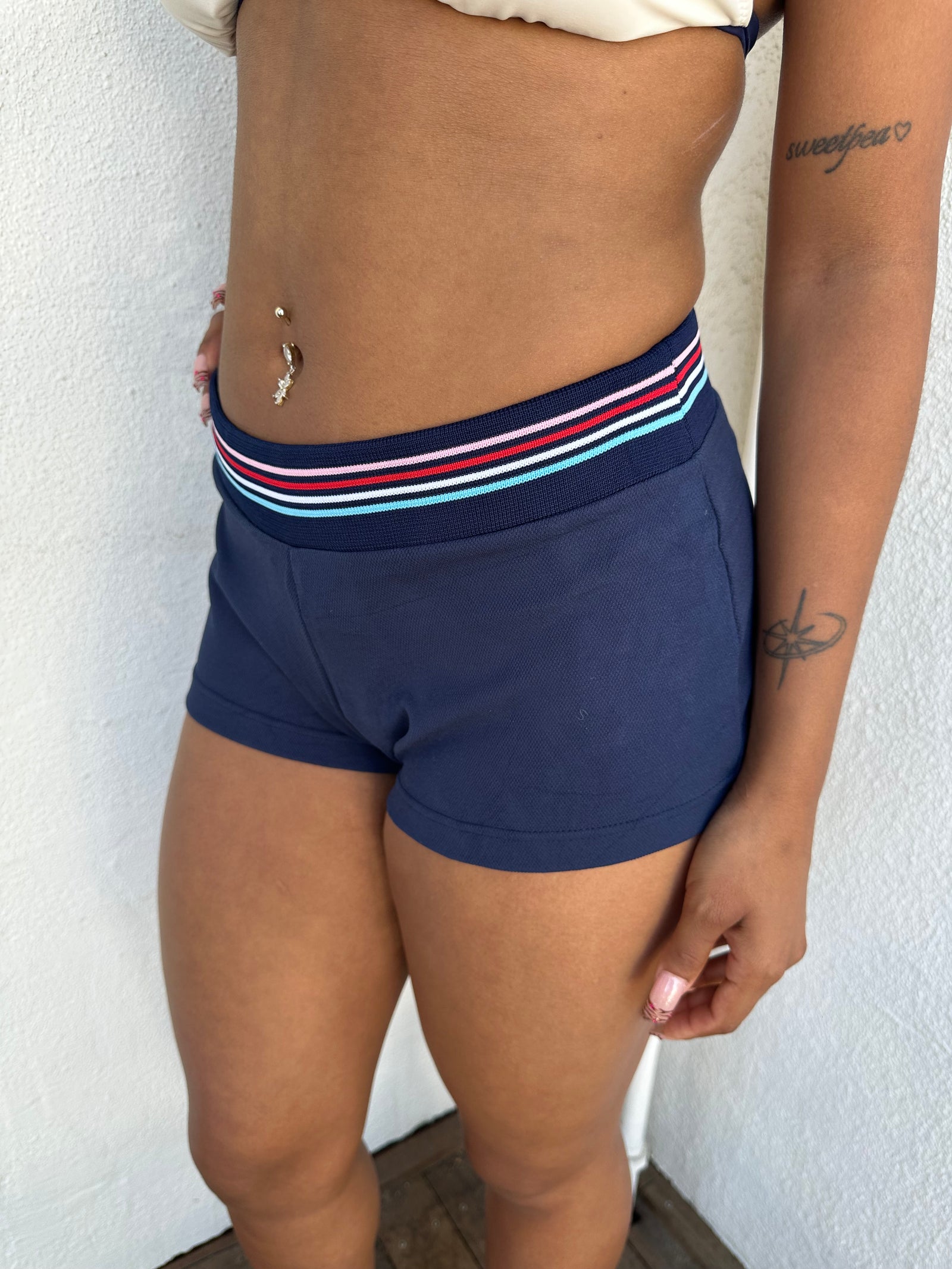 Woman Dressed in Y2K 00s Navy printed booty shorts featuring a navy base with “Roco Nails” printed across the bum. 