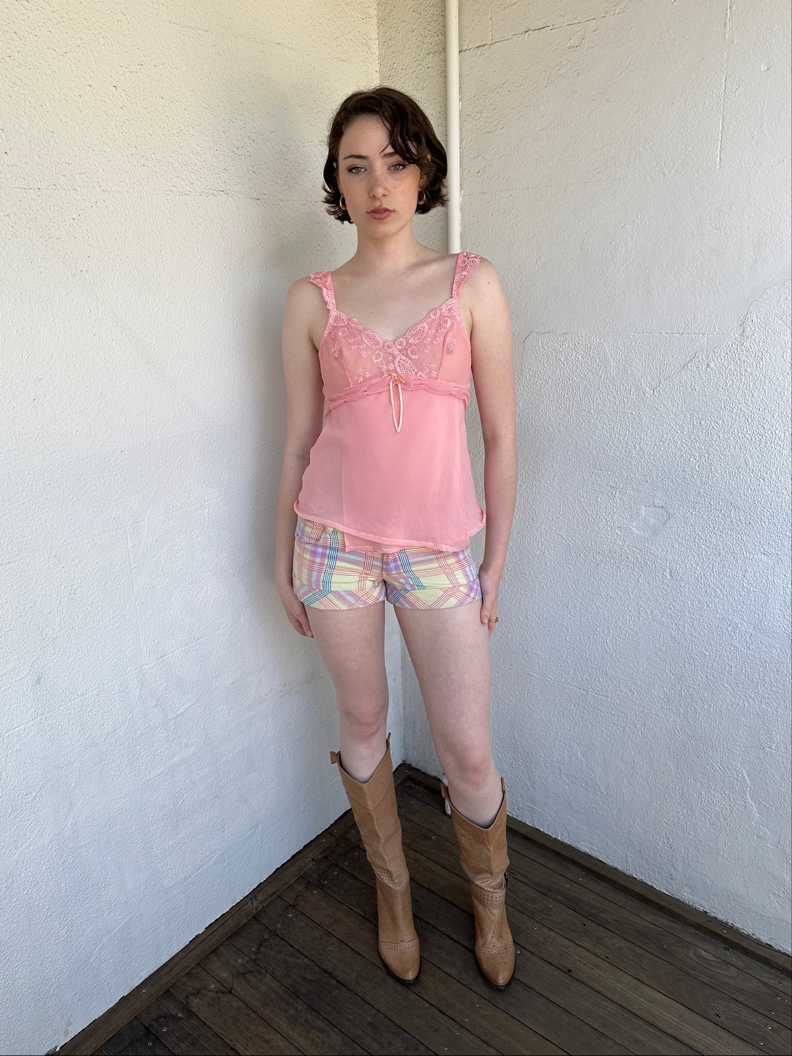 Woman Dressed in Y2K Pastel multicoloured tartan shorts featuring a fitted booty-style silhouette with a chunky pastel yellow button feature.