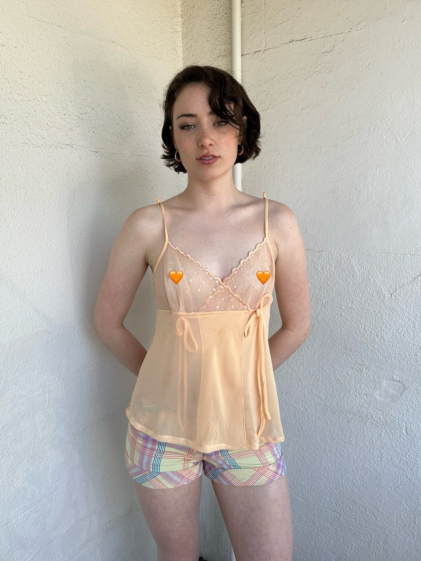 Woman Dressed in Y2K Pastel orange embroidered mesh cami top featuring a soft pastel orange tone with a crossover two-tie system at the front.