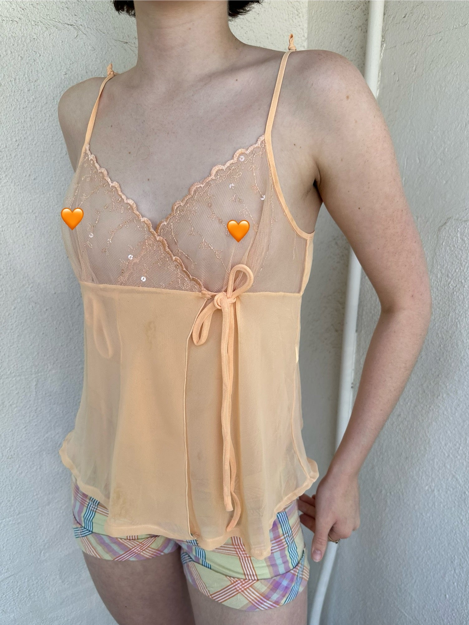Woman Dressed in Y2K Pastel orange embroidered mesh cami top featuring a soft pastel orange tone with a crossover two-tie system at the front.