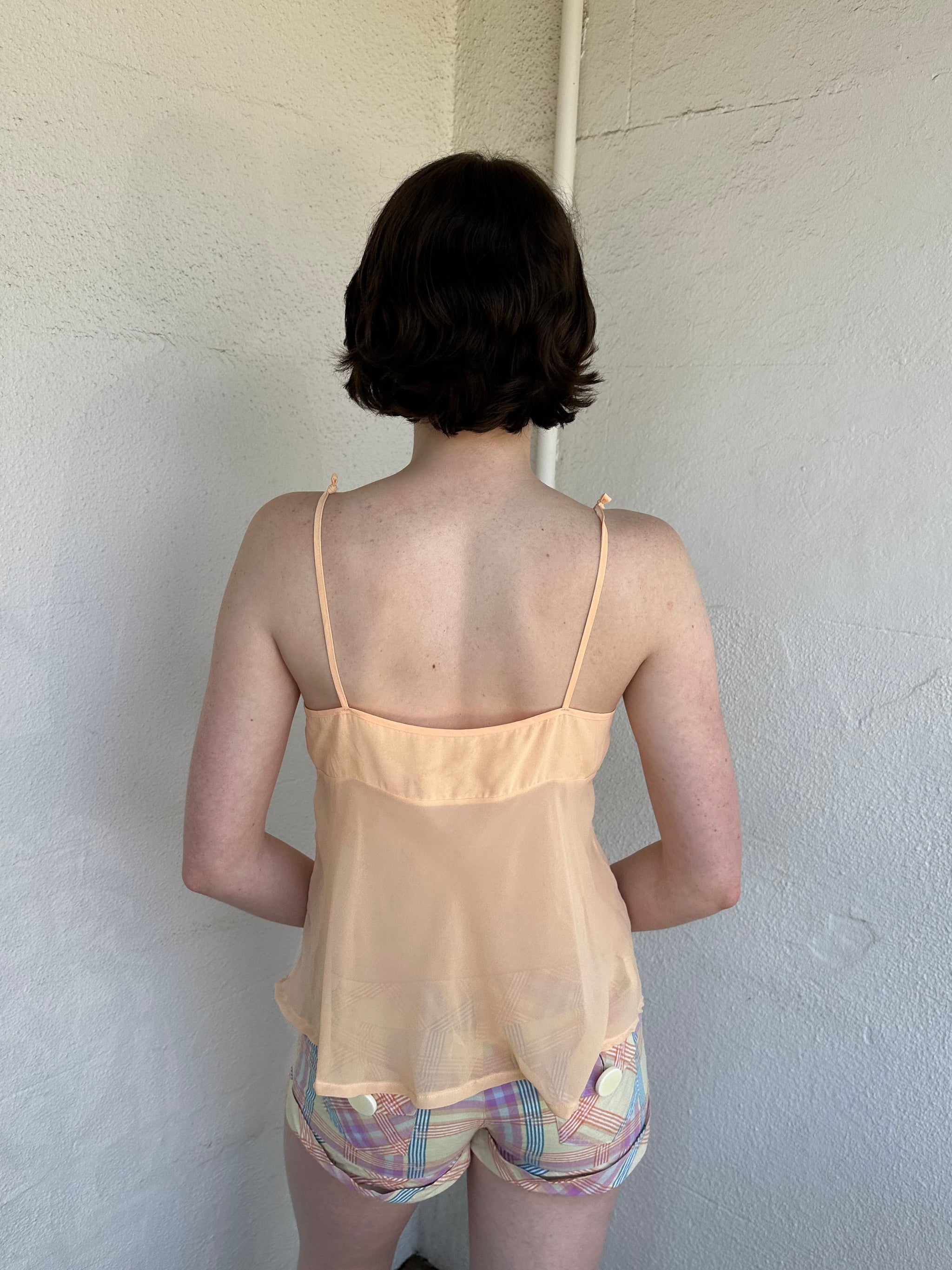 Woman Dressed in Y2K Pastel orange embroidered mesh cami top featuring a soft pastel orange tone with a crossover two-tie system at the front.