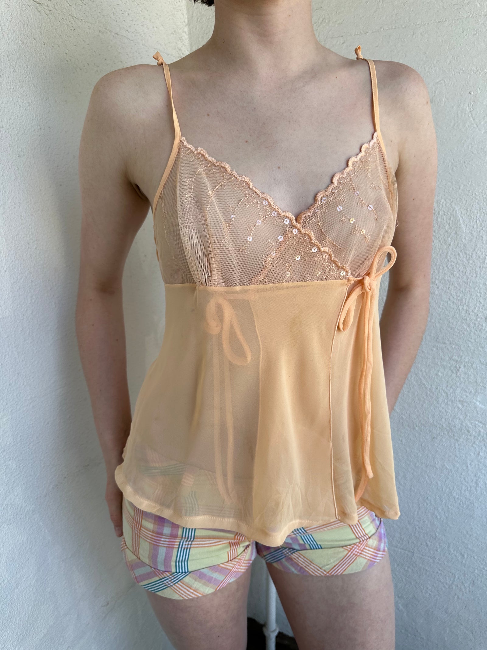 Woman Dressed in Y2K Pastel orange embroidered mesh cami top featuring a soft pastel orange tone with a crossover two-tie system at the front.