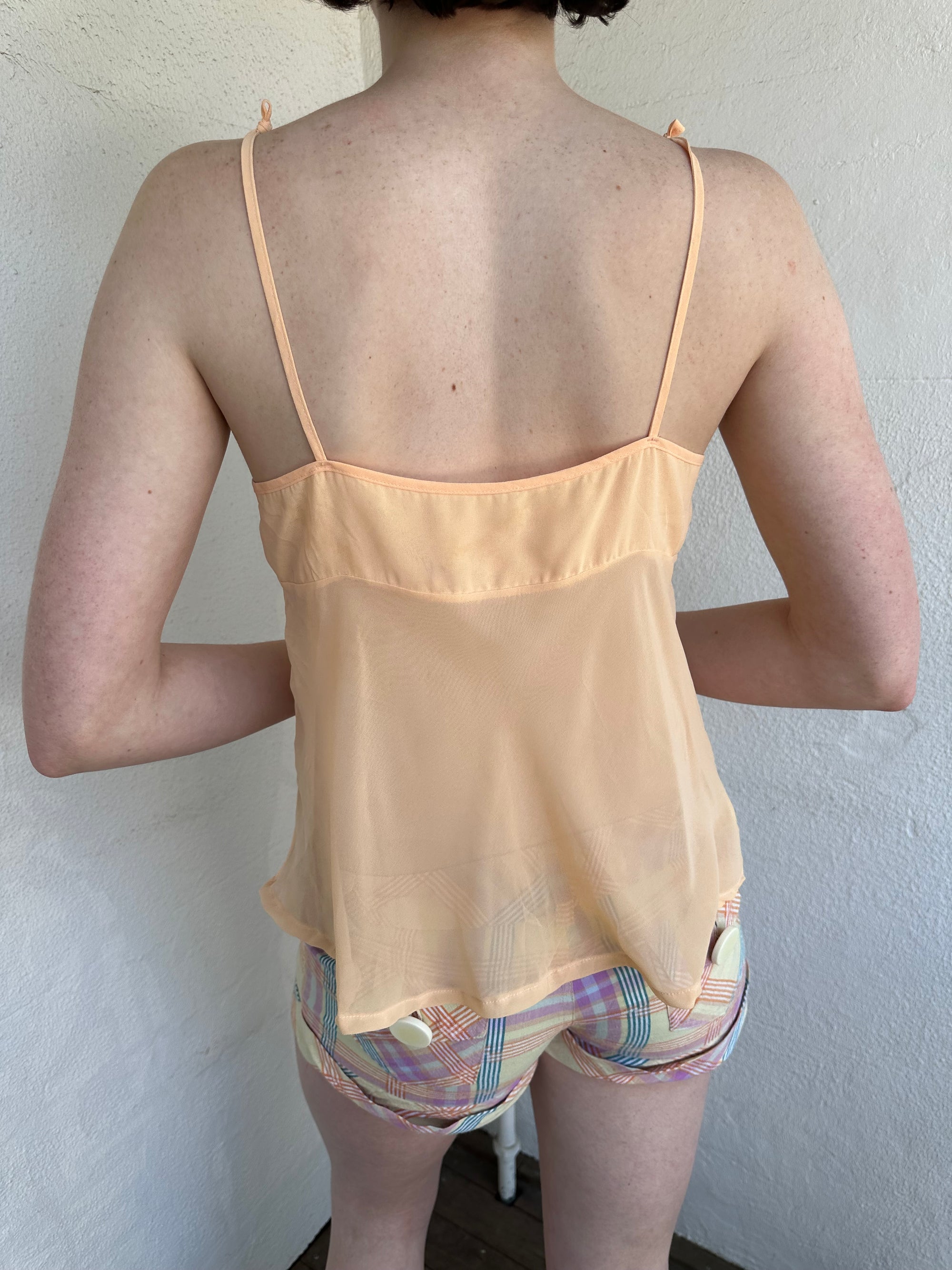 Woman Dressed in Y2K Pastel orange embroidered mesh cami top featuring a soft pastel orange tone with a crossover two-tie system at the front.