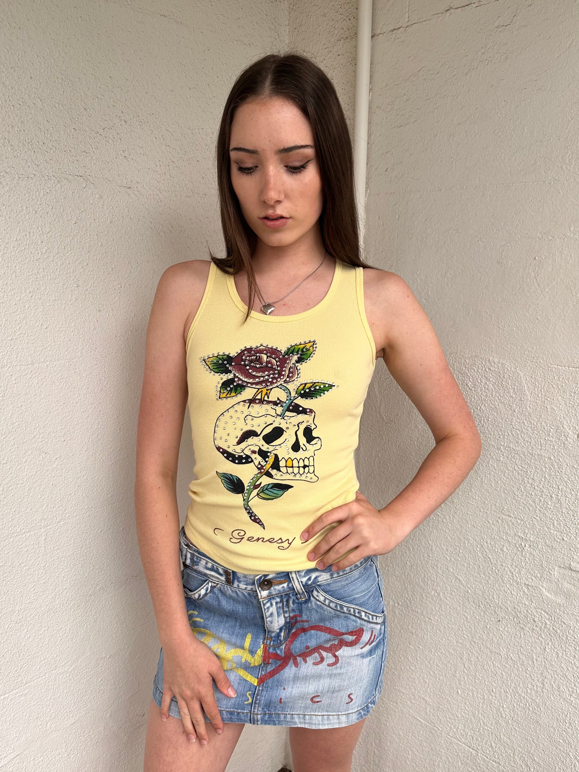 Women wearing a 00s Y2K Pastel yellow Y2K graphic tank from Genesy featuring a skull and flower print with rhinestone accents. 