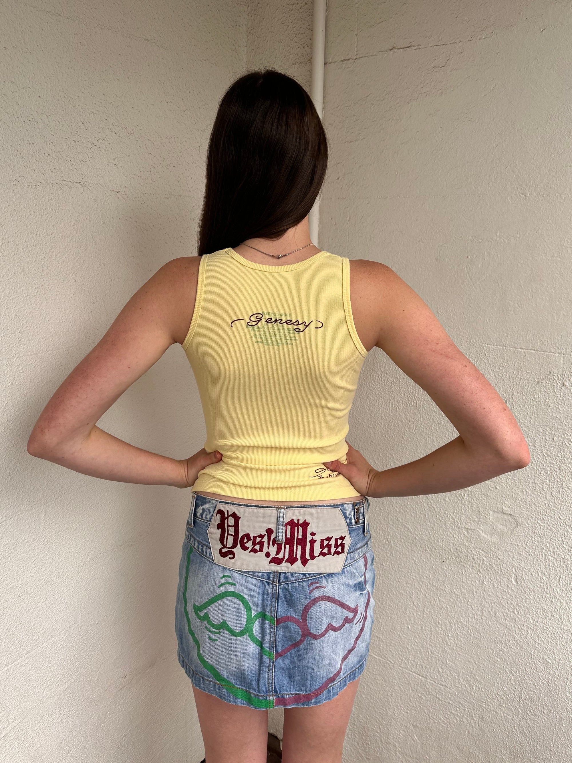 Women wearing a 00s Y2K Pastel yellow Y2K graphic tank from Genesy featuring a skull and flower print with rhinestone accents. 