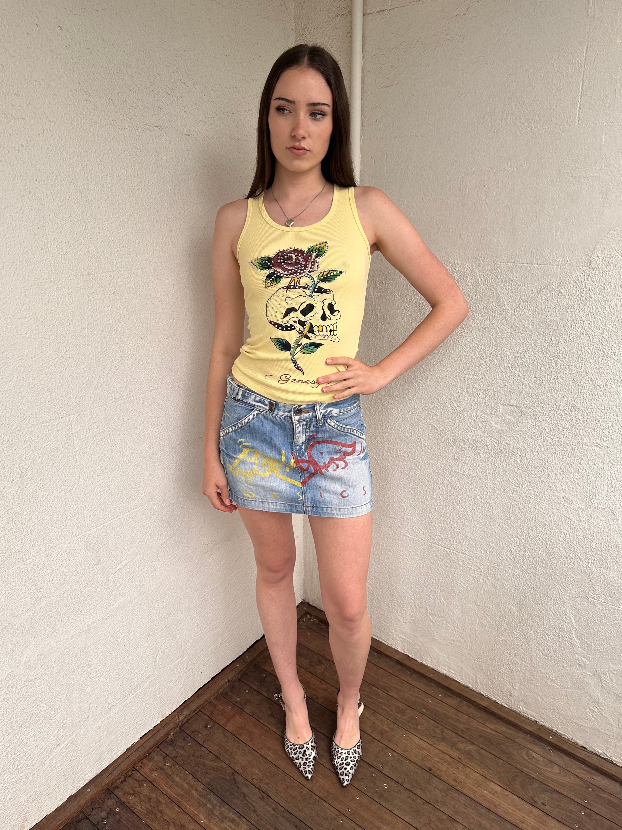 Women wearing a 00s Y2K Pastel yellow Y2K graphic tank from Genesy featuring a skull and flower print with rhinestone accents. 
