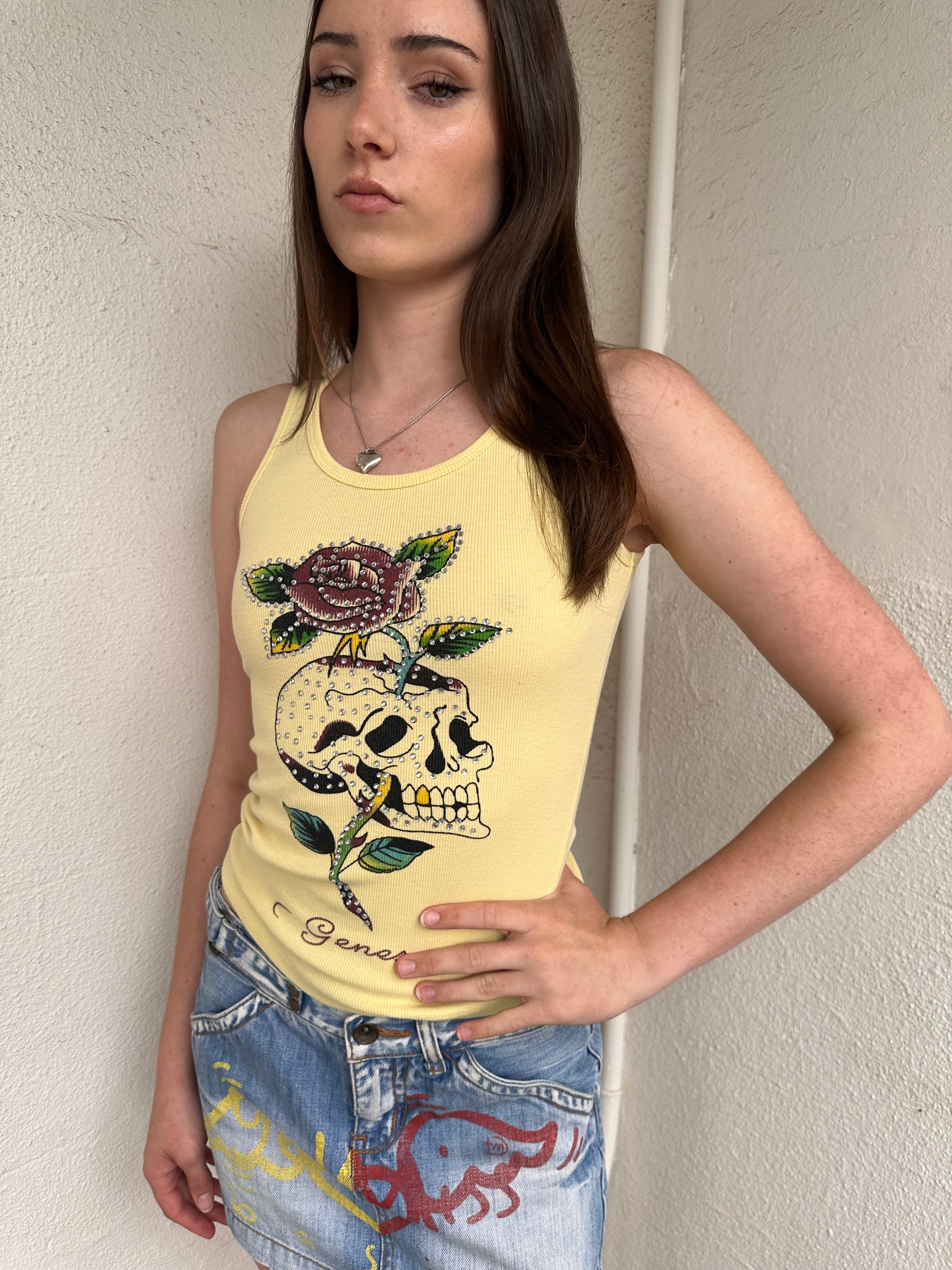 Women wearing a 00s Y2K Pastel yellow Y2K graphic tank from Genesy featuring a skull and flower print with rhinestone accents. 