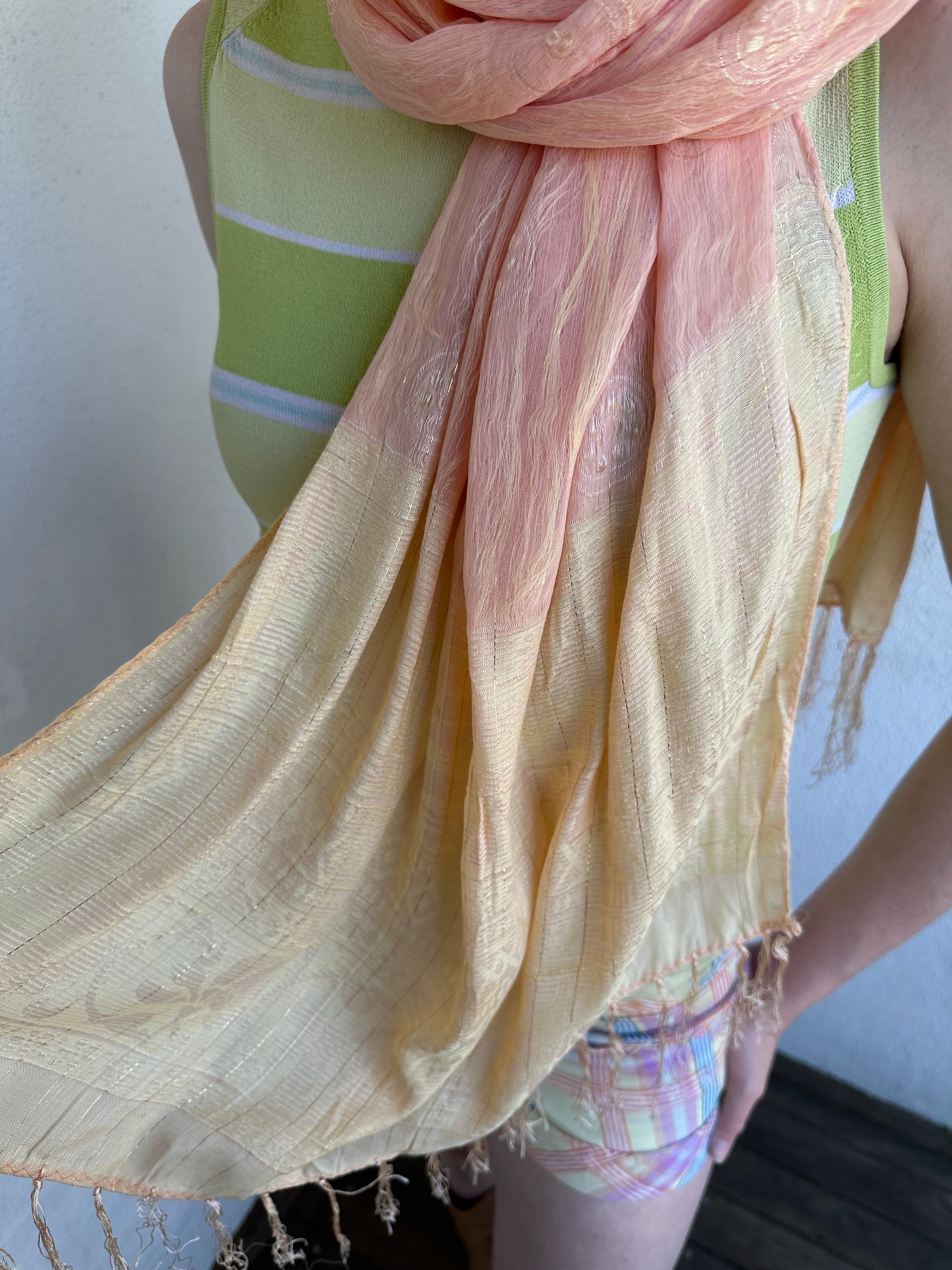 Woman Dressed in Y2K Peach and gold patterned festival scarf featuring a sheer silk-style fabric with a small circular pattern and gold fleck detailing throughout.