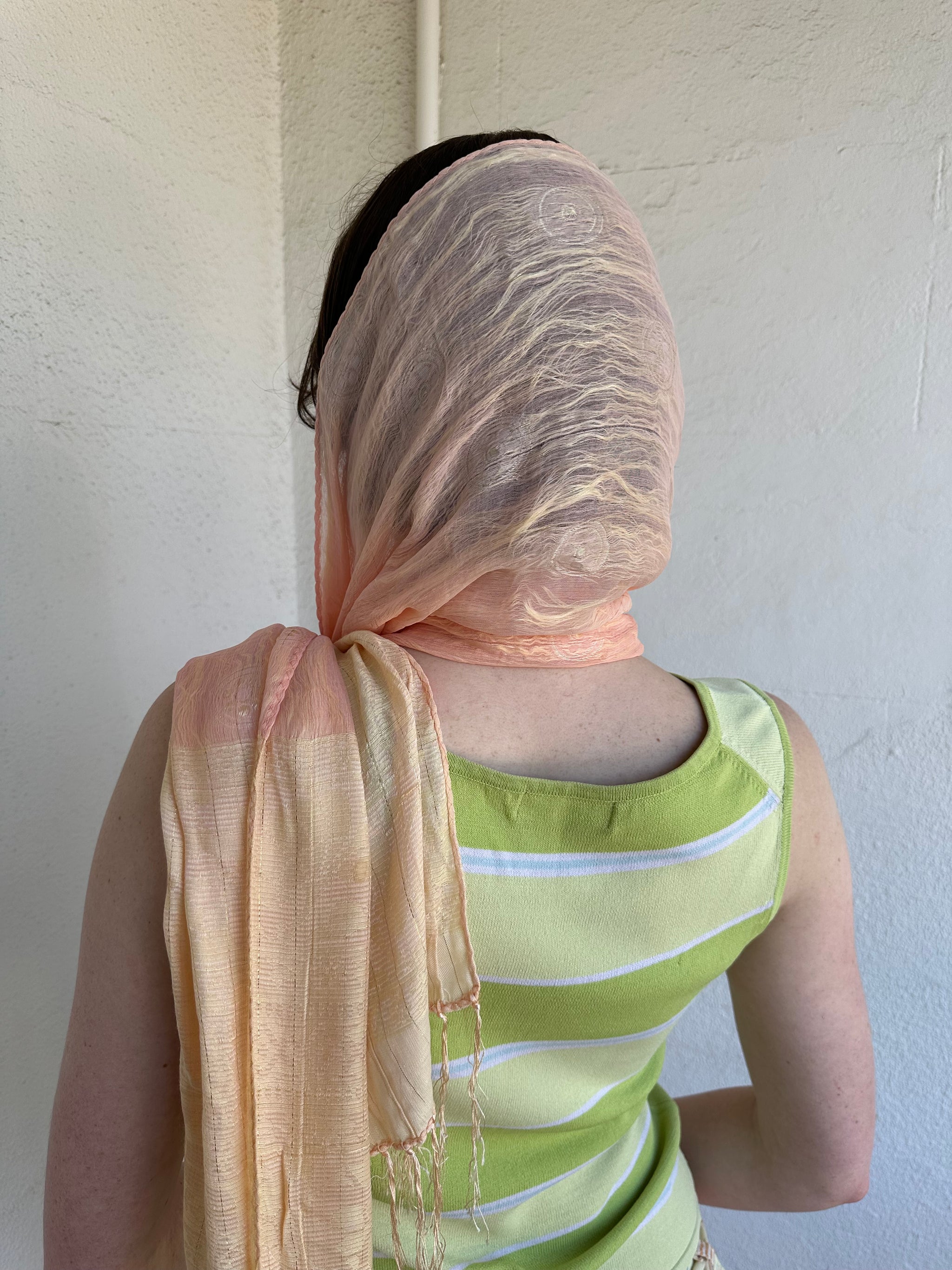 Woman Dressed in Y2K Peach and gold patterned festival scarf featuring a sheer silk-style fabric with a small circular pattern and gold fleck detailing throughout.