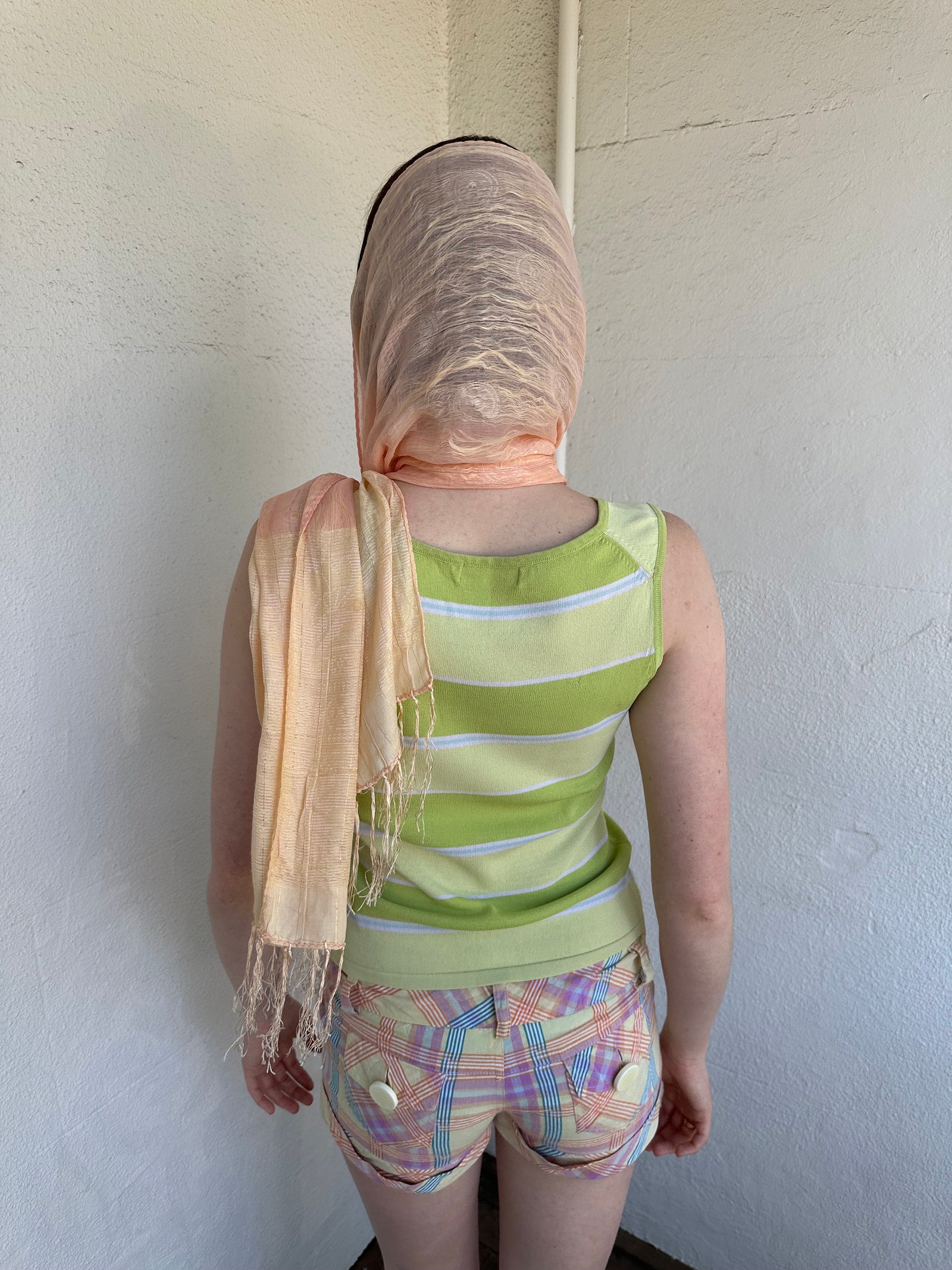 Woman Dressed in Y2K Peach and gold patterned festival scarf featuring a sheer silk-style fabric with a small circular pattern and gold fleck detailing throughout.