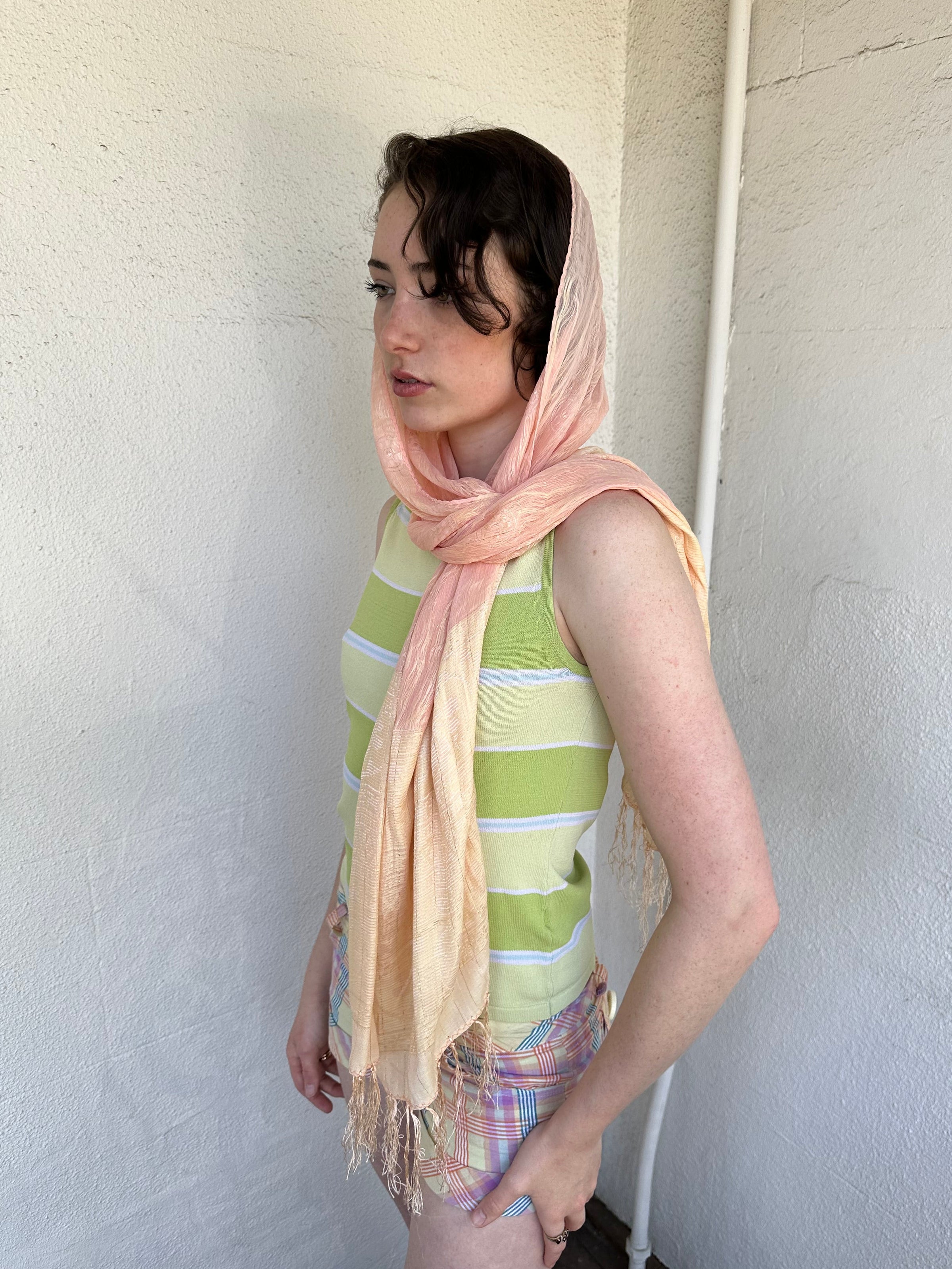 Woman Dressed in Y2K Peach and gold patterned festival scarf featuring a sheer silk-style fabric with a small circular pattern and gold fleck detailing throughout.
