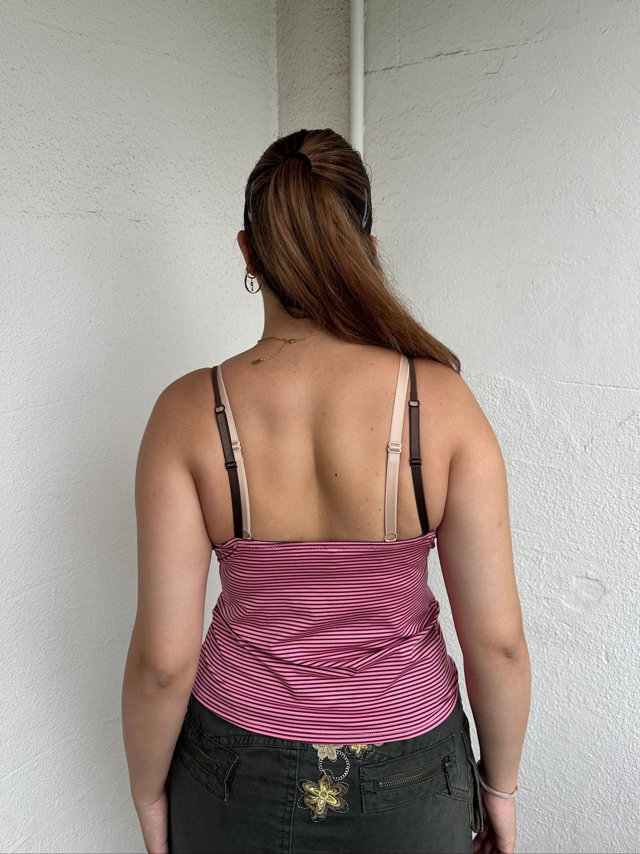 Woman Dressed in Y2K 00s Pink and brown stripe cami featuring a striped design in pink and brown tones with a pink rosette detail at the centre.