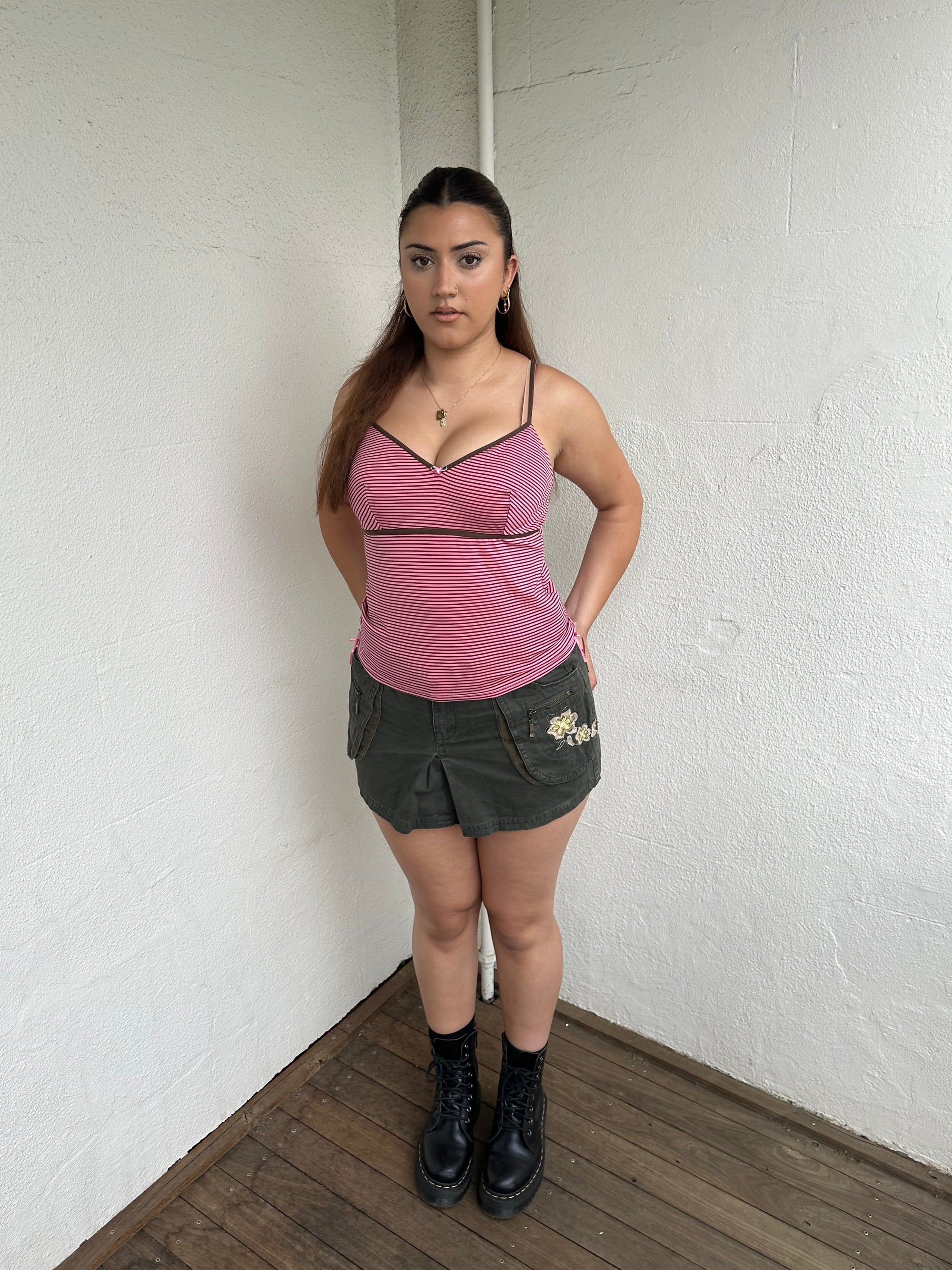 Woman Dressed in Y2K 00s Pink and brown stripe cami featuring a striped design in pink and brown tones with a pink rosette detail at the centre.
