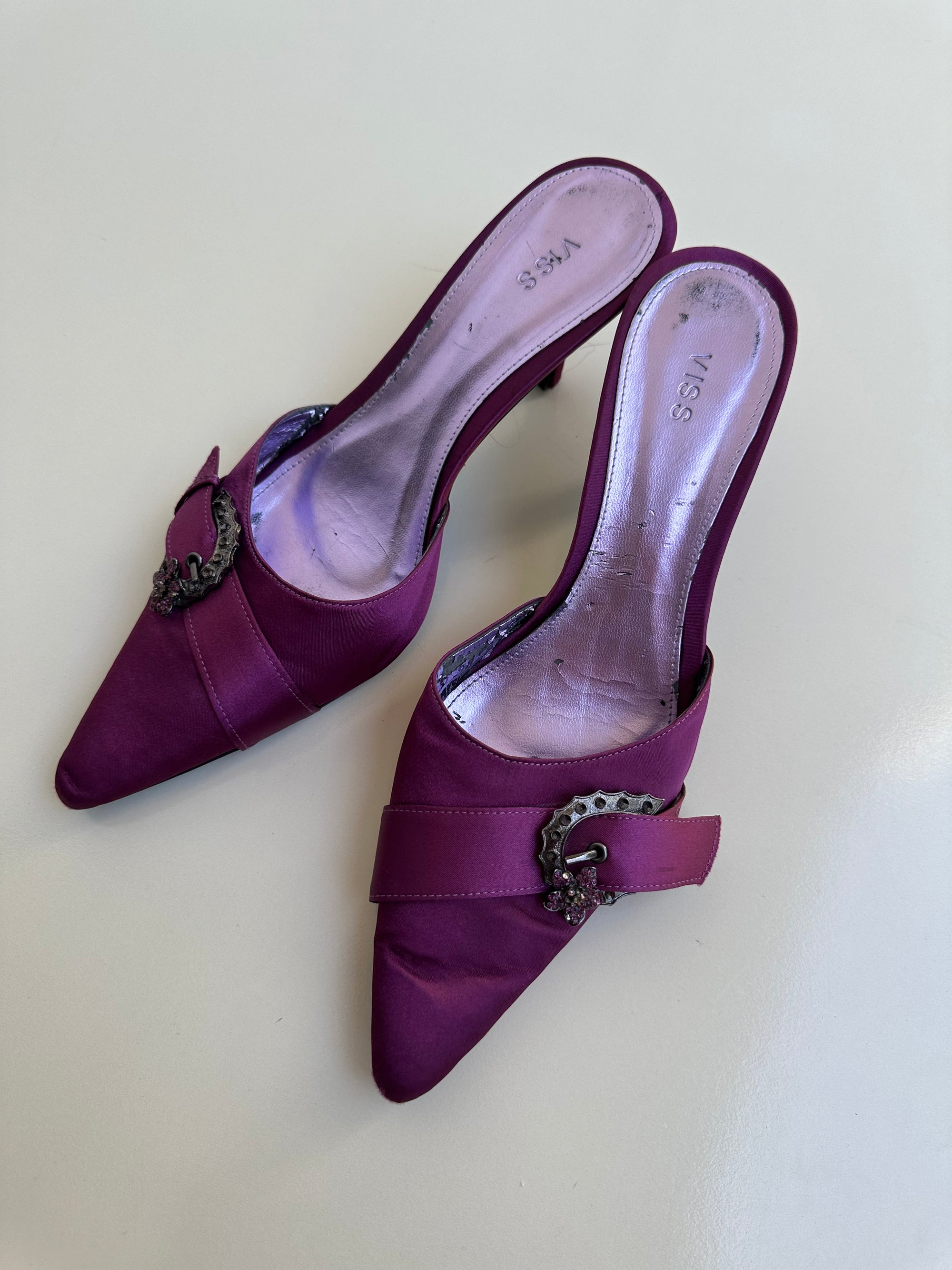 Pair of purple high-heeled shoes with decorative bows on a light background