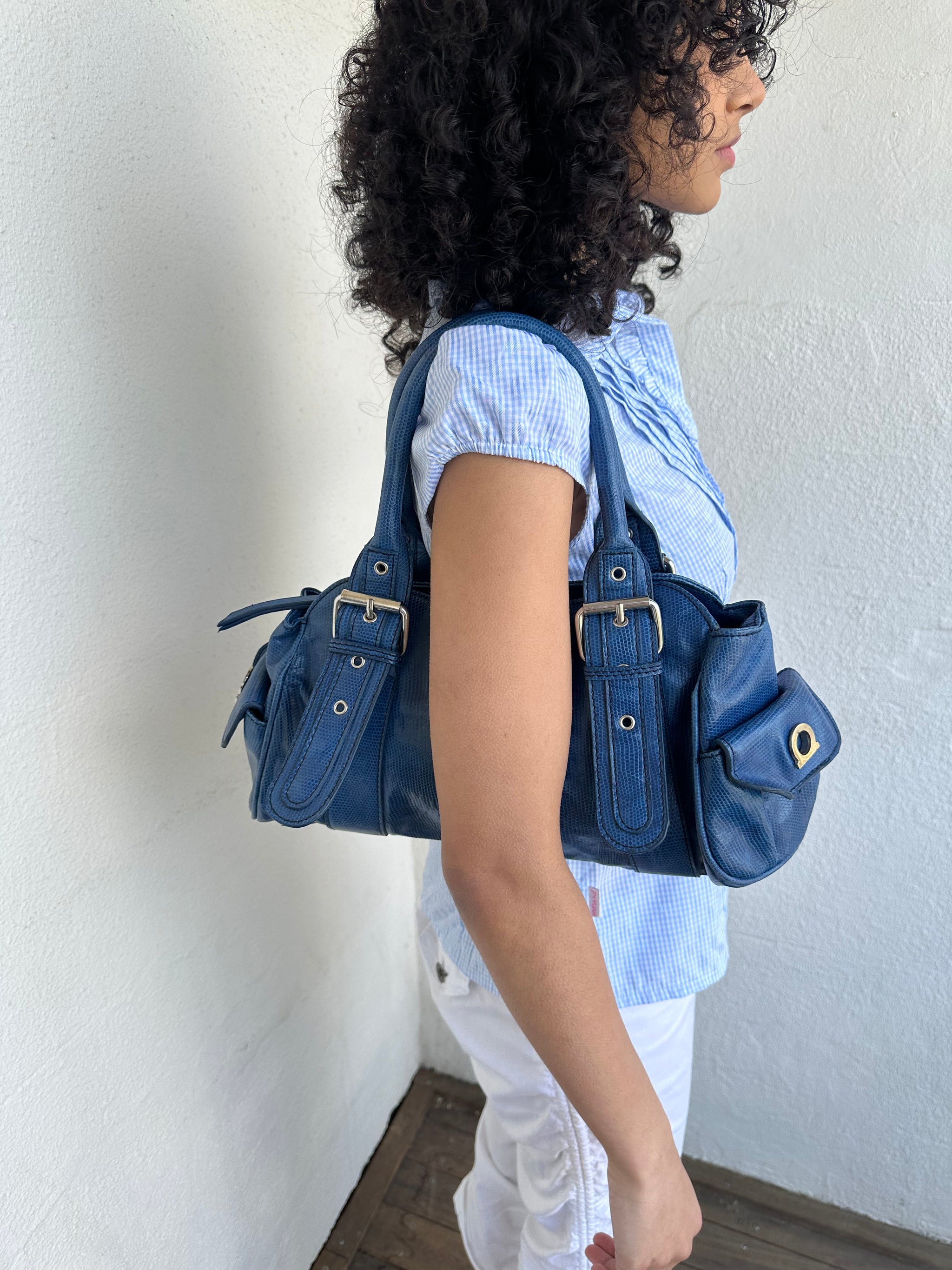 Woman wearing a Y2K 90s Royal blue faux leather shoulder bag with silver hardware and a sleek, structured shape. 