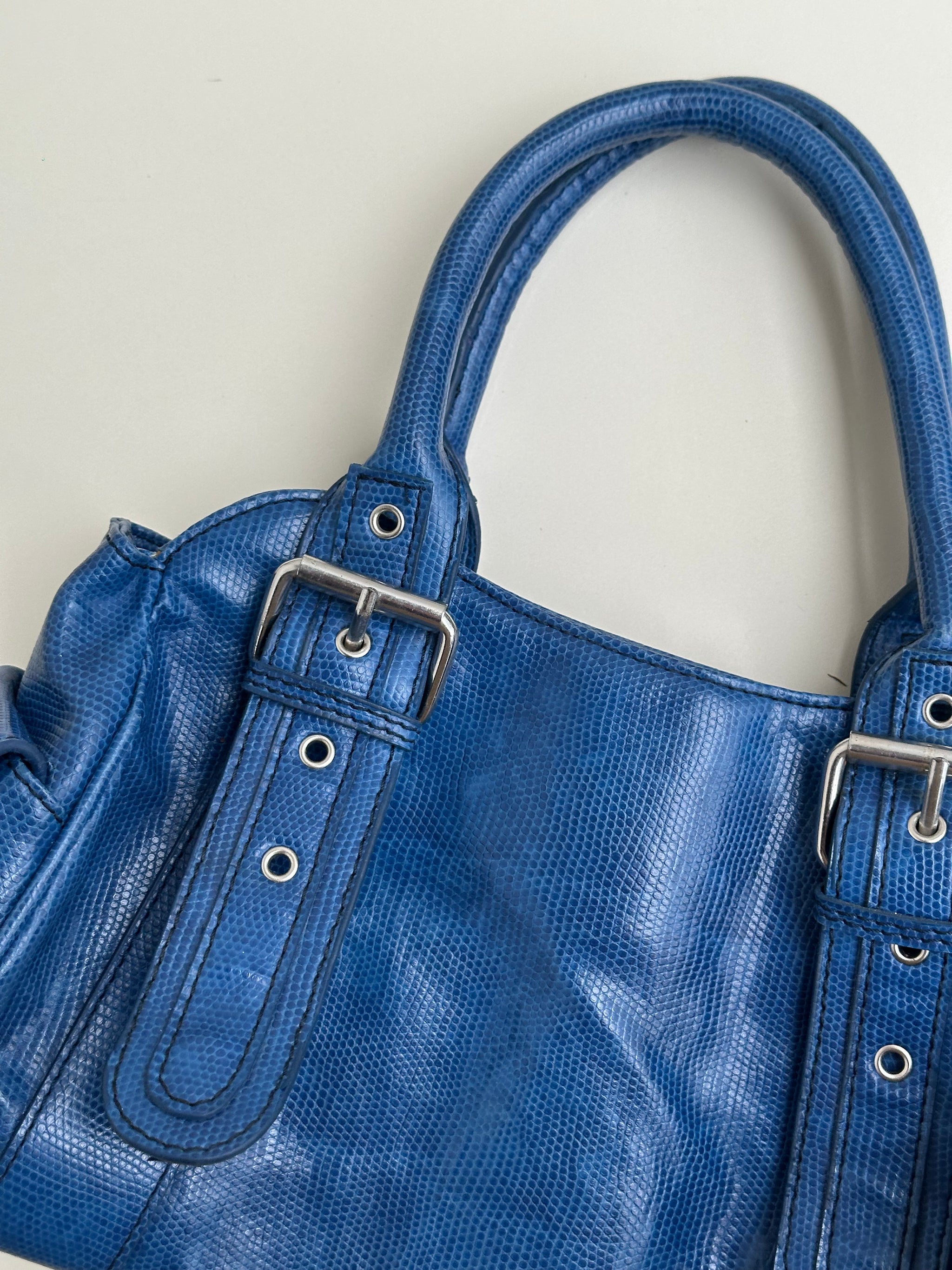 Woman wearing a Y2K 90s Royal blue faux leather shoulder bag with silver hardware and a sleek, structured shape. 