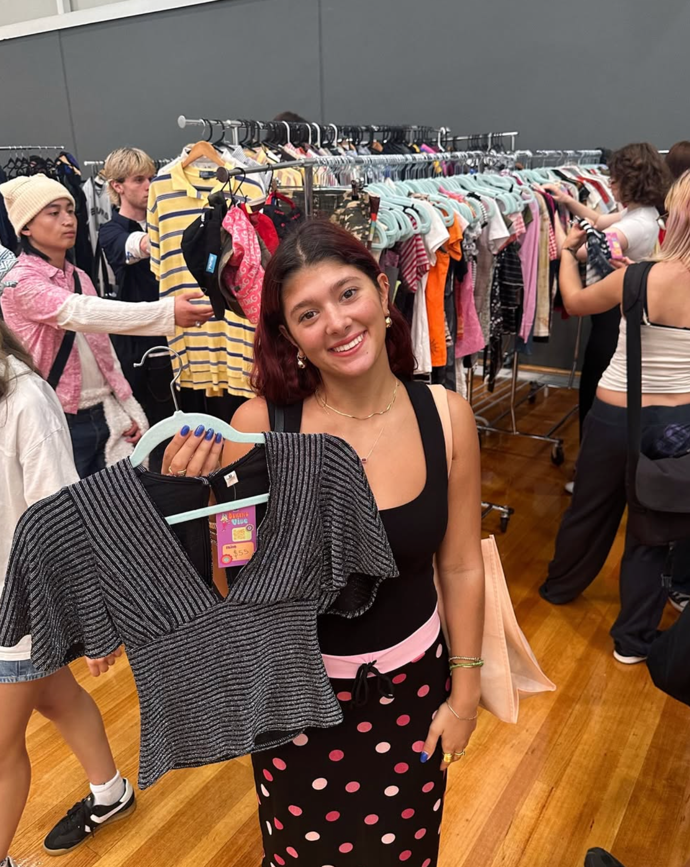 Woman holding a black and white striped top at market with racks of clothes and people around.