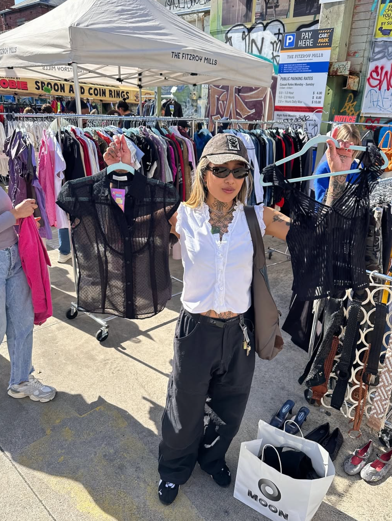 Person shopping at an outdoor flea market with clothes on racks and a tent.