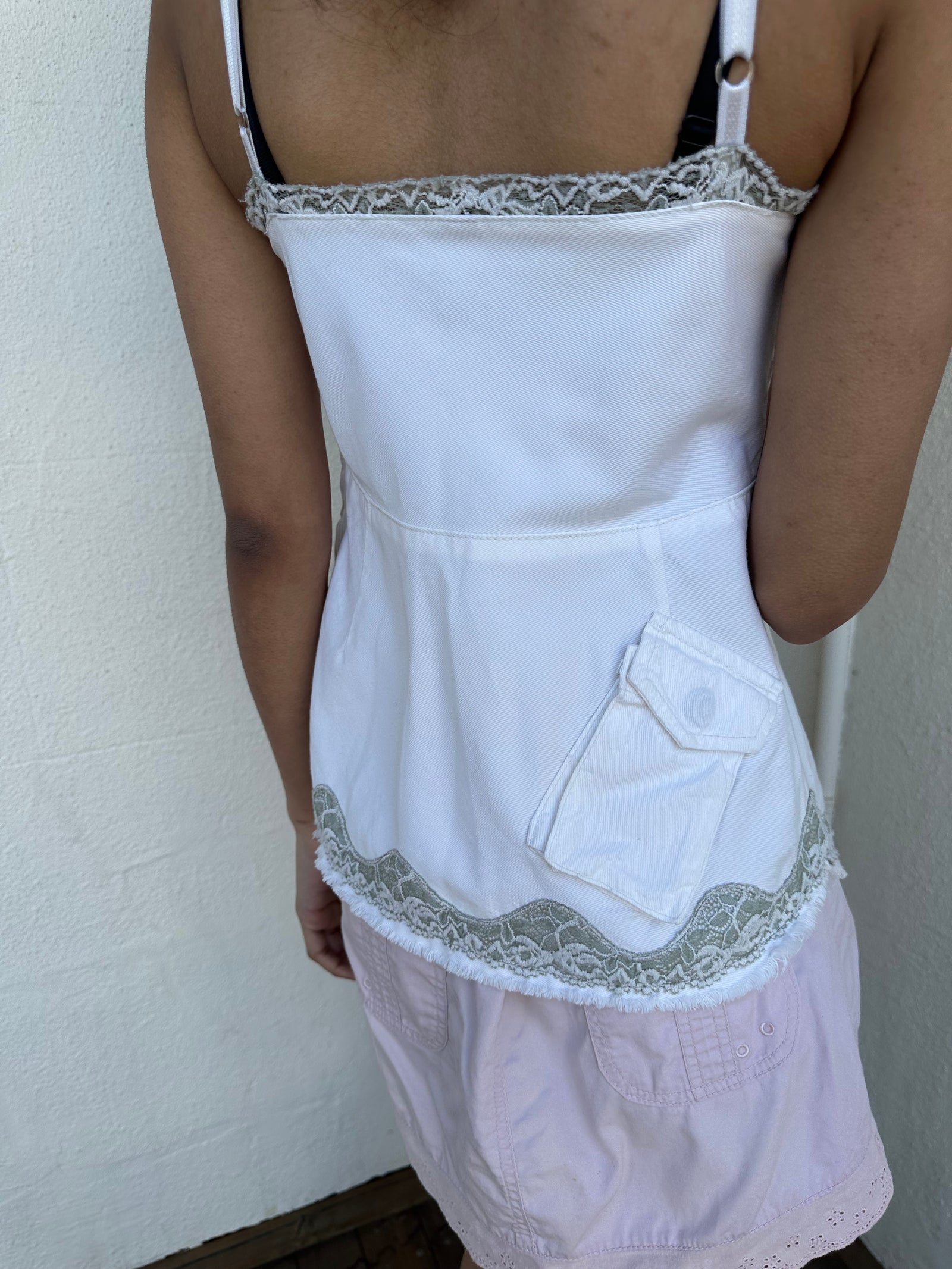 Woman wearing a Y2K 90s White denim fitted cami top with grey lace trim and a small patch pocket on the back sized for a flip phone! 