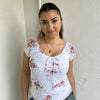 Woman Dressed in Y2K 00s White floral 90s milkmaid style top featuring a white base with a red rose floral pattern throughout.