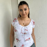 Woman Dressed in Y2K 00s White floral 90s milkmaid style top featuring a white base with a red rose floral pattern throughout.
