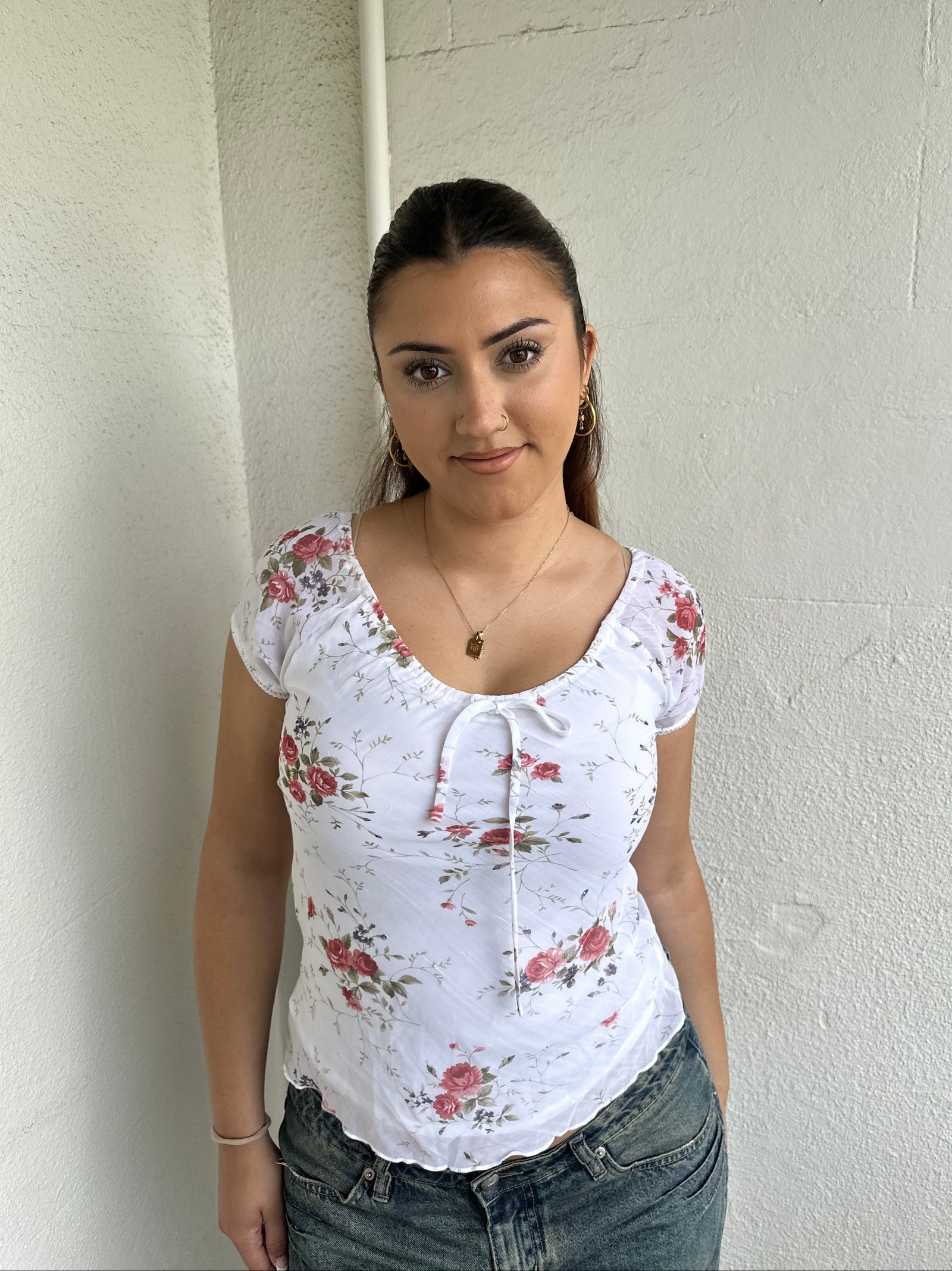 Woman Dressed in Y2K 00s White floral 90s milkmaid style top featuring a white base with a red rose floral pattern throughout.