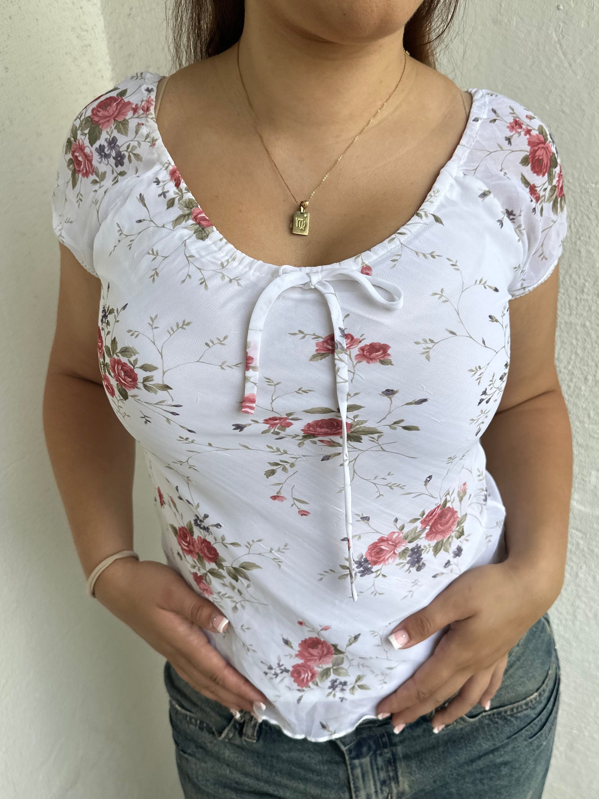 Woman Dressed in Y2K 00s White floral 90s milkmaid style top featuring a white base with a red rose floral pattern throughout.