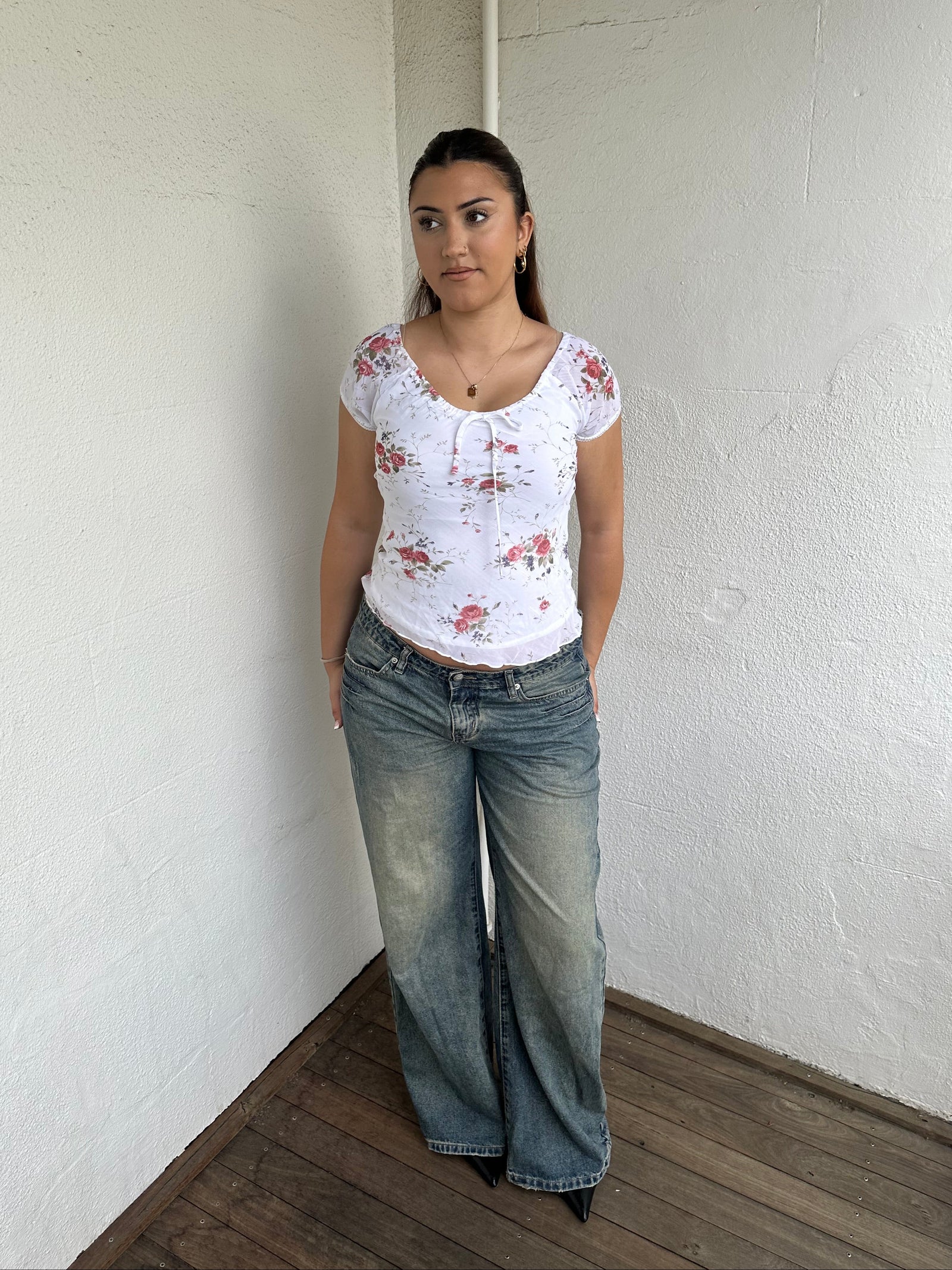 Woman Dressed in Y2K 00s White floral 90s milkmaid style top featuring a white base with a red rose floral pattern throughout.