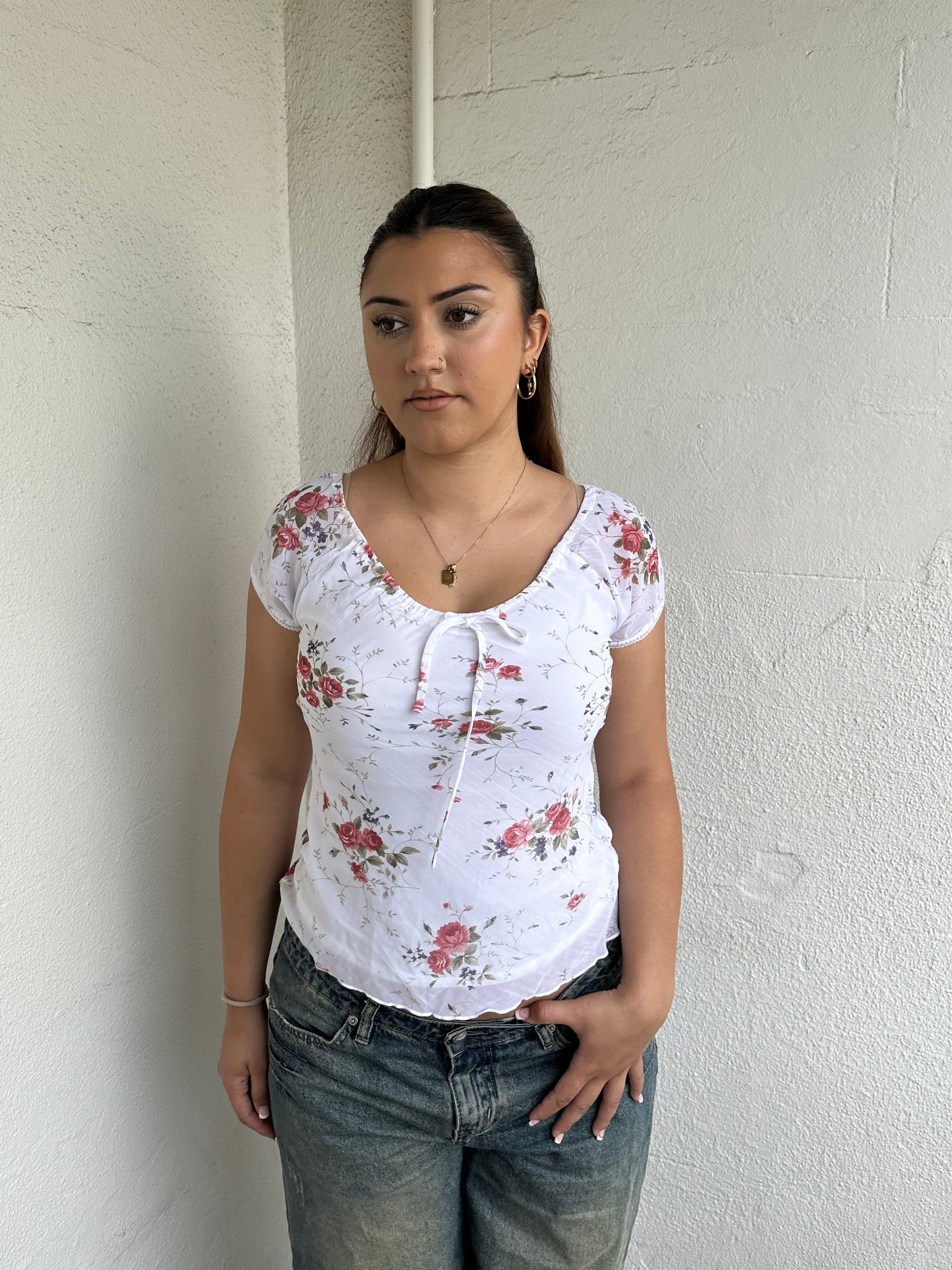 Woman Dressed in Y2K 00s White floral 90s milkmaid style top featuring a white base with a red rose floral pattern throughout.