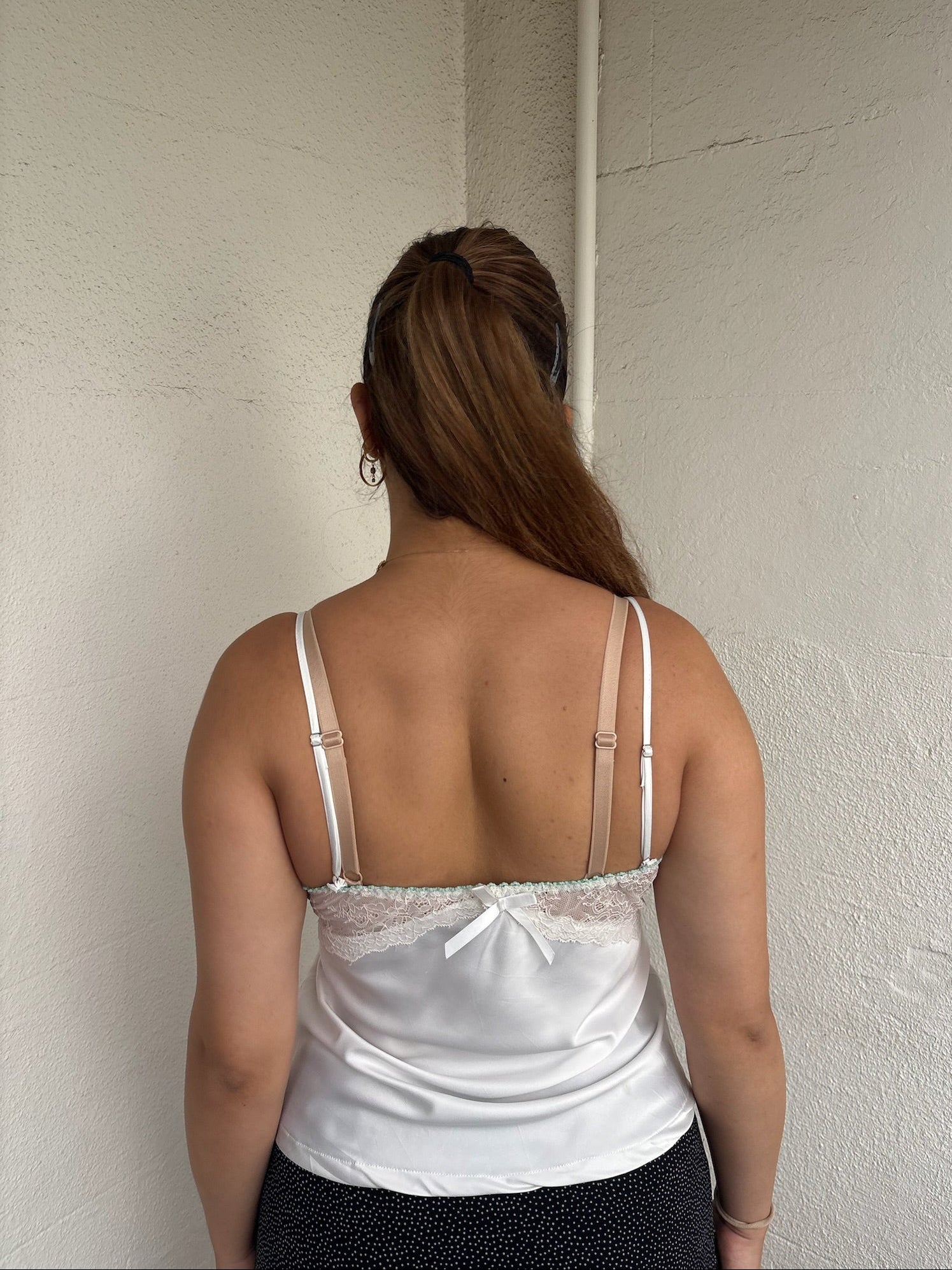 Woman Dressed in Y2K 00sWhite floral embroidered cami featuring a white and green embroidered flower design on the bust and a smooth satin body.