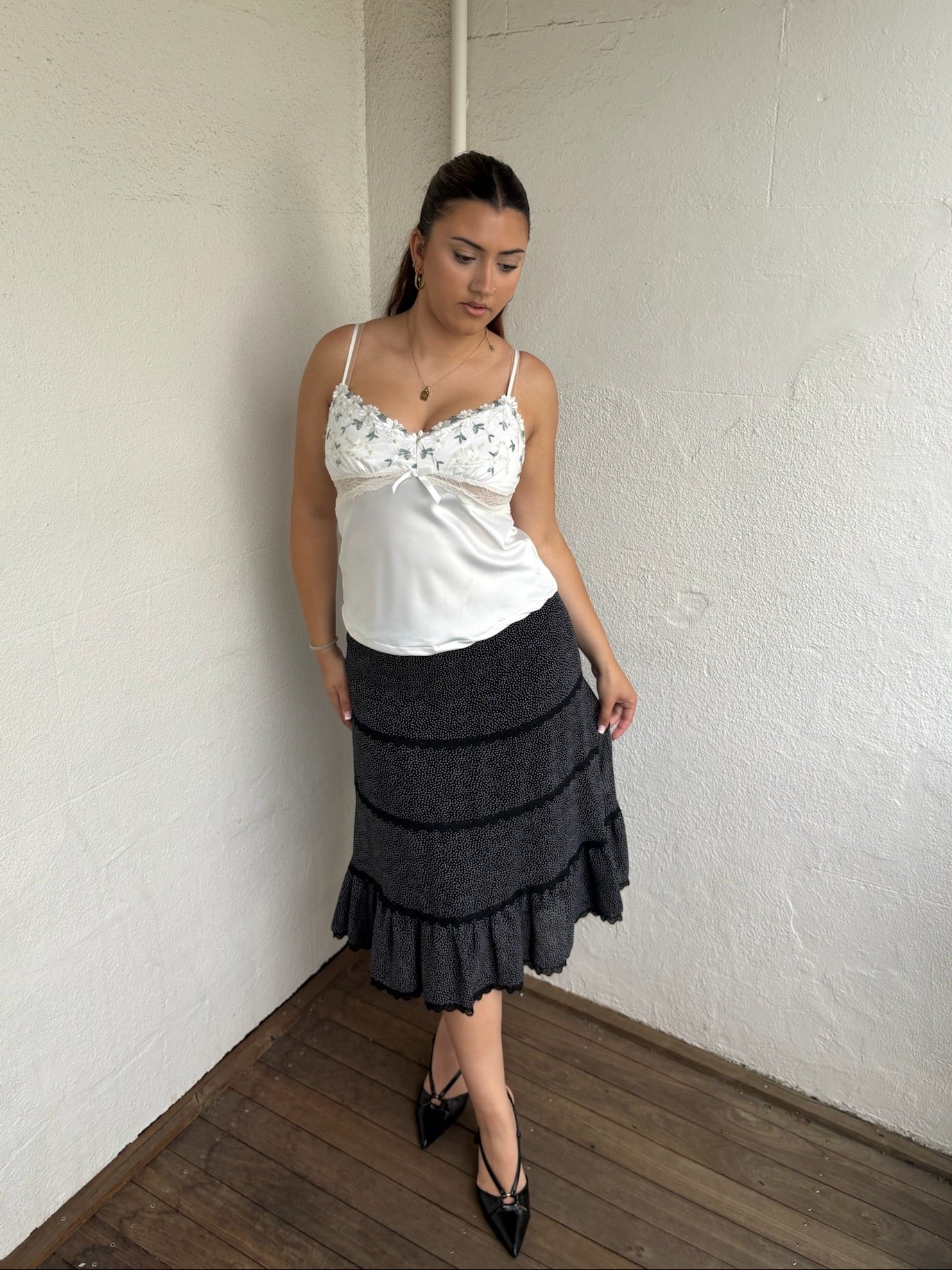 Woman Dressed in Y2K 00sWhite floral embroidered cami featuring a white and green embroidered flower design on the bust and a smooth satin body.