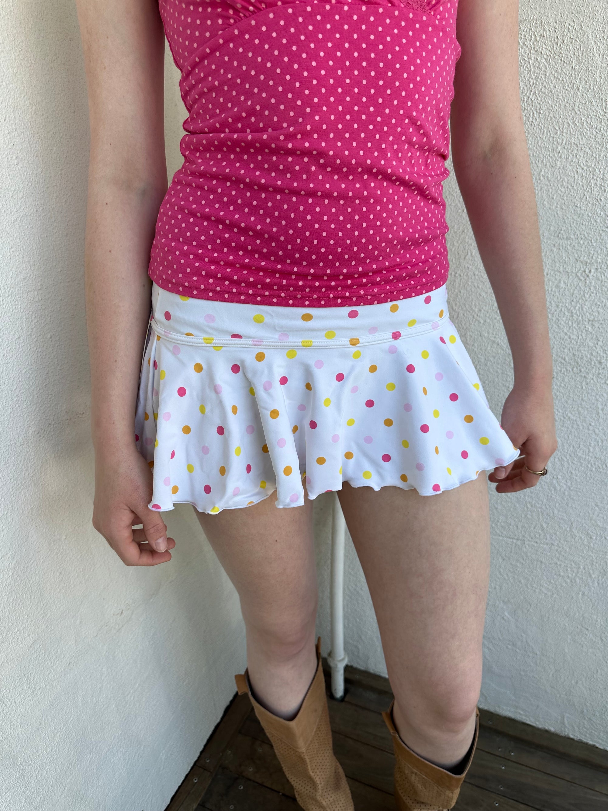 Woman Dressed in Y2K White and multicoloured polkadot mini skirt featuring a crisp white base with pink, yellow, and orange polkadots throughout.