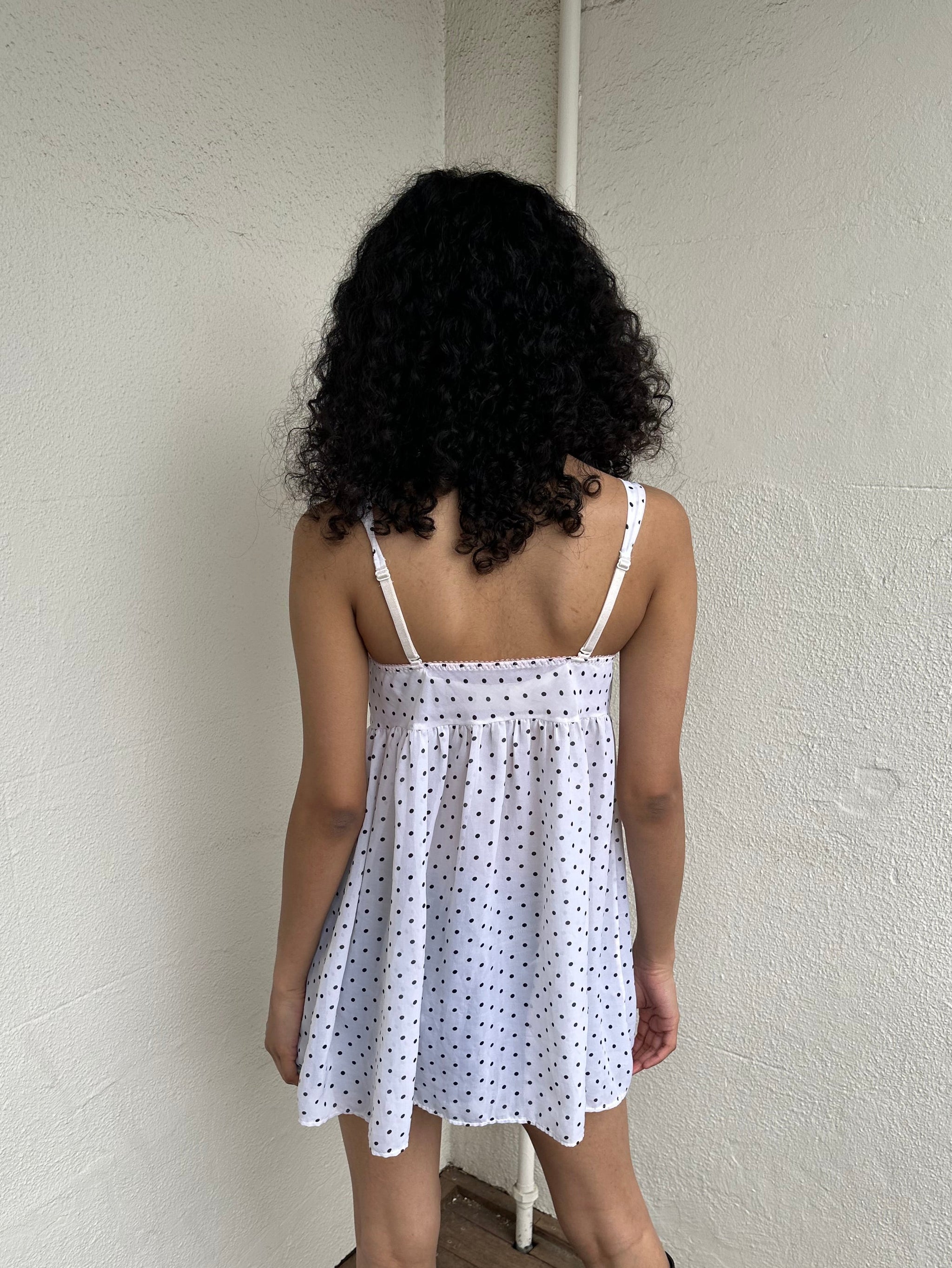 Woman Dressed in Y2K 00s White polkadot babydoll dress featuring a white base with classic polkadot detailing 
